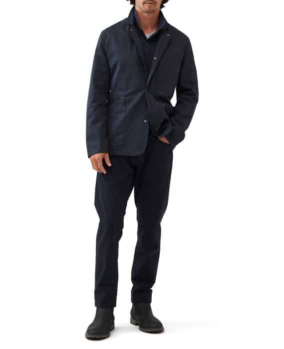 A person is wearing a dark blue jacket over a shirt and matching pants. They have dark shoes and are standing against a white background. Their face is not shown.