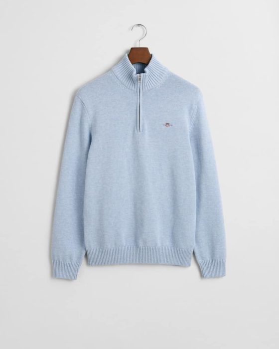 Light blue sweater with a half-zip design, featuring ribbed cuffs and hem. It has a small embroidered emblem on the left chest. The sweater is hung on a wooden hanger against a plain white background.