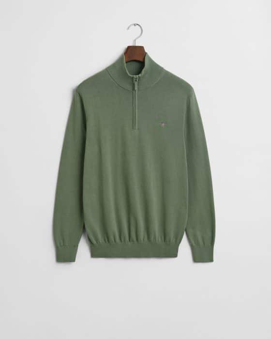 A green quarter-zip sweater is hanging on a wooden hanger against a white background. It features ribbed cuffs and hem, with a small embroidered logo on the left chest.