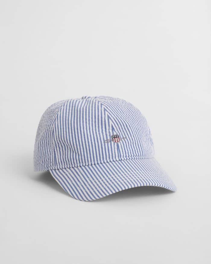 A blue and white striped baseball cap with a small embroidered logo featuring a red and white shield and blue stripes. The cap is on a plain white background.