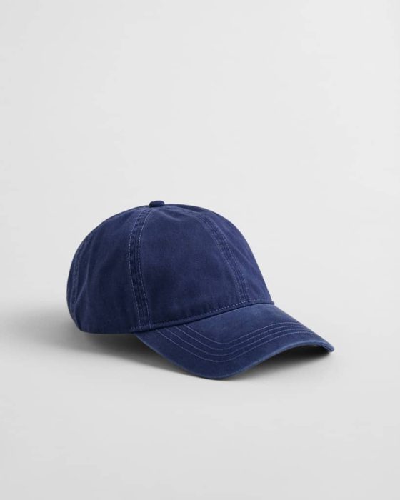 A navy blue baseball cap on a plain light gray background. The cap features white stitching along its seams and a curved brim.