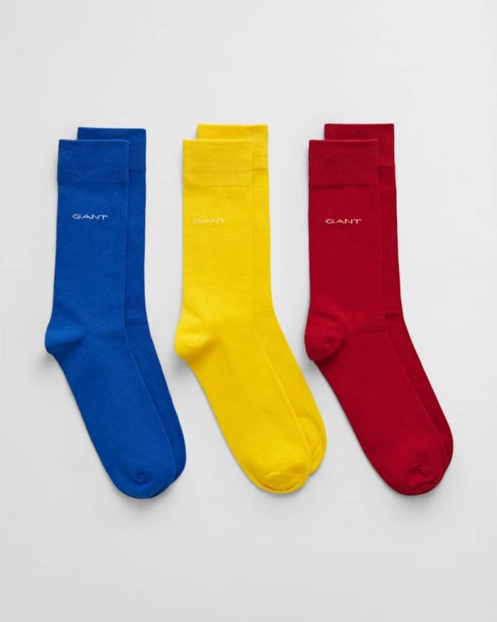 Three pairs of socks are displayed against a white background. The socks are solid colors: blue, yellow, and red. Each sock has the word GANT embroidered near the top.