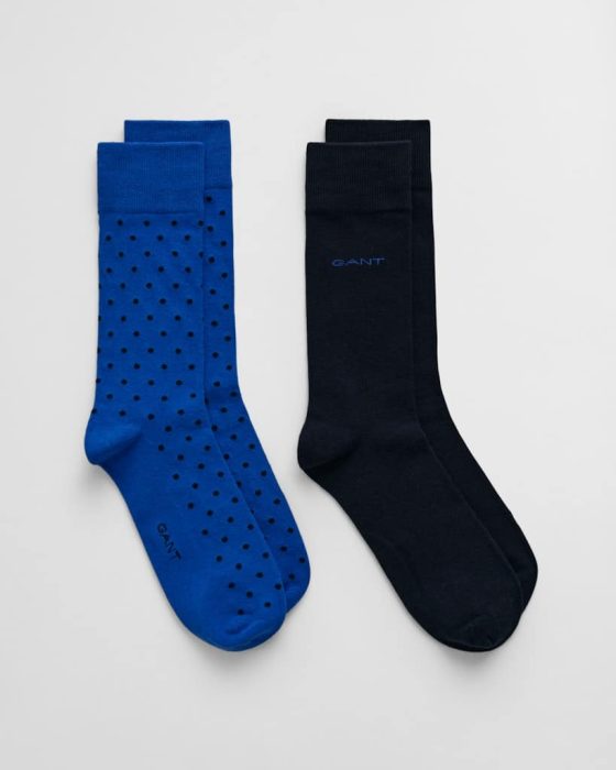 A pair of blue socks with black polka dots and a pair of solid black socks are placed against a plain white background. Both pairs have the word GANT written on them.