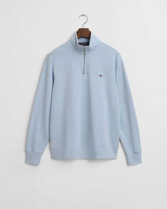 A light blue pullover with a quarter-zip front and a small embroidered logo on the left chest, hanging on a wooden hanger against a white background.