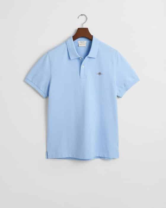 Light blue polo shirt on a wooden hanger against a white background. The shirt features short sleeves, a collar, and a small embroidered logo on the left chest.