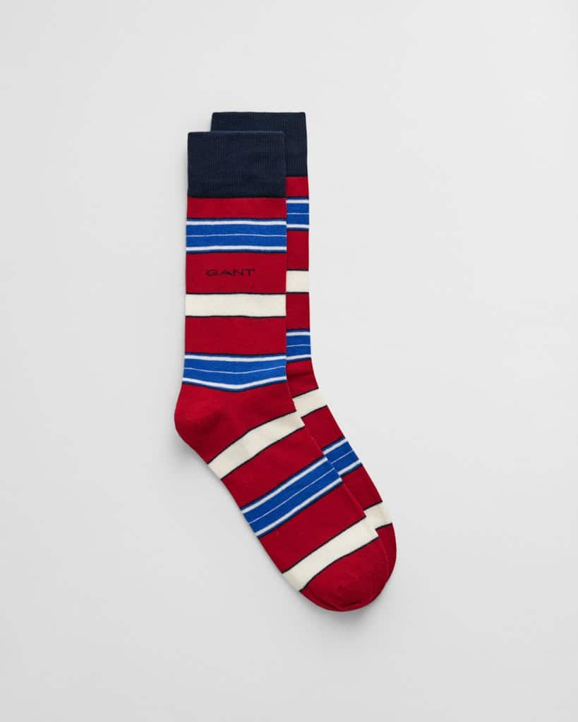 A pair of socks featuring a pattern of red, white, and blue horizontal stripes. One sock is laid flat on top of the other, with GANT printed on the side of each sock. The toe and heel are dark blue.