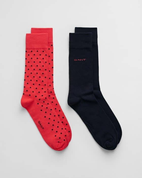 Two pairs of socks on a light background. The left pair is red with black polka dots, and the right pair is solid black. Both have the word GANT printed near the toes.