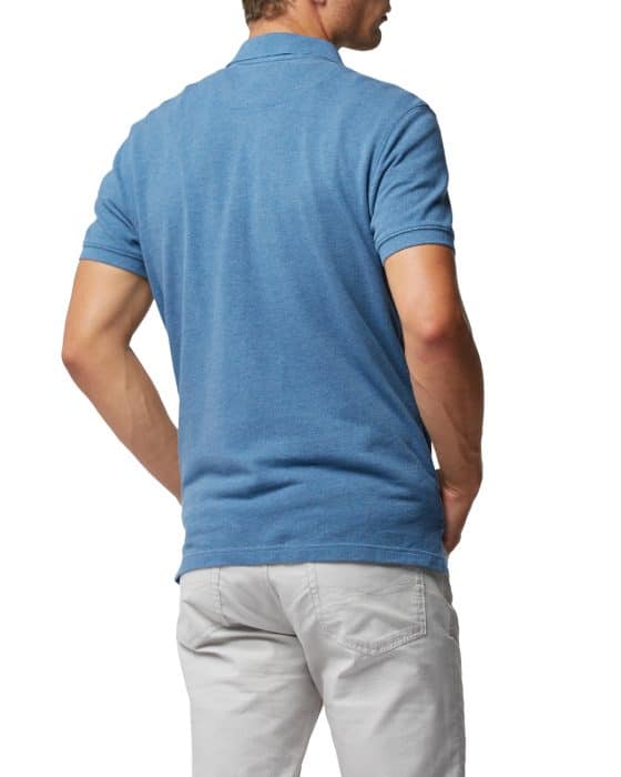 Man wearing a blue short-sleeve polo shirt and light gray pants, viewed from the back. His hands are in his pockets, and he is standing against a plain white background.