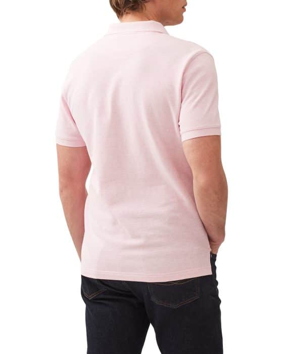 Rear view of a person wearing a light pink polo shirt and dark jeans. The person is standing with hands in their pockets, looking to the side. The background is plain white.