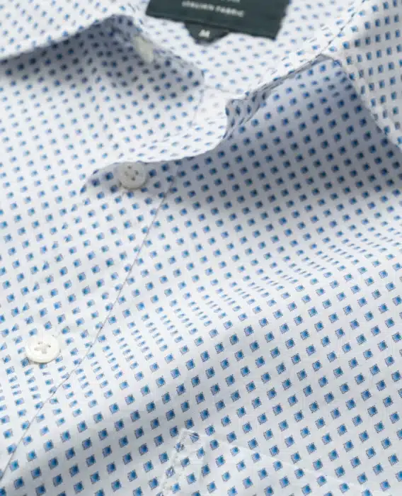 Close-up of a white button-up shirt with a pattern of small blue diamonds. The fabric appears smooth and lightweight, with a subtle sheen. The buttons are white, and the shirt has a standard collar.