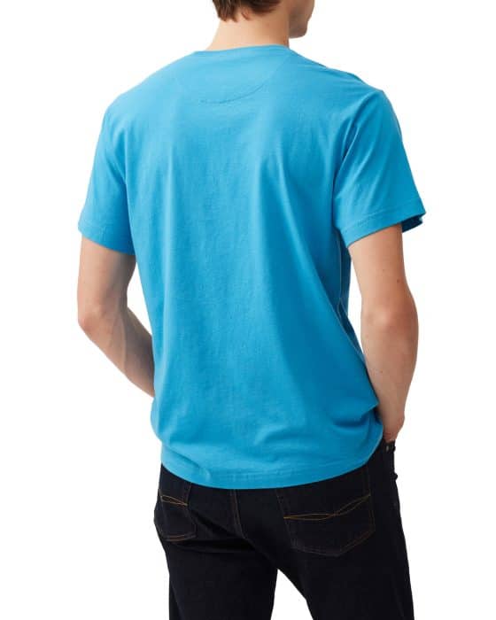 A person wearing a bright blue T-shirt and dark jeans is standing with their back to the camera. The individual has their hands in their pockets and their head turned slightly to the side.