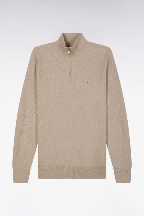 A beige, long-sleeve sweater with a high collar and a quarter-length zipper down the front. The sweater features a small, subtle logo on the left chest and ribbed cuffs and hem. The background is plain white.