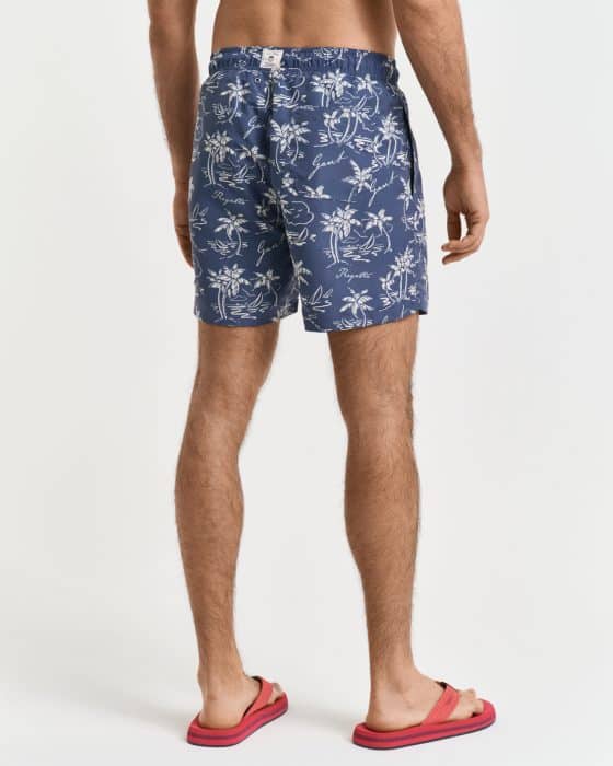 A person is standing with their back to the camera, wearing blue shorts with a white floral pattern and red flip-flops. The background is plain white.