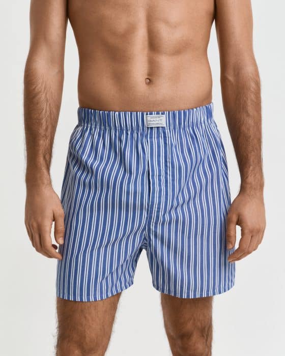 A person stands against a plain background, wearing blue and white vertically striped boxer shorts. The person is shirtless and has their arms relaxed at their sides.