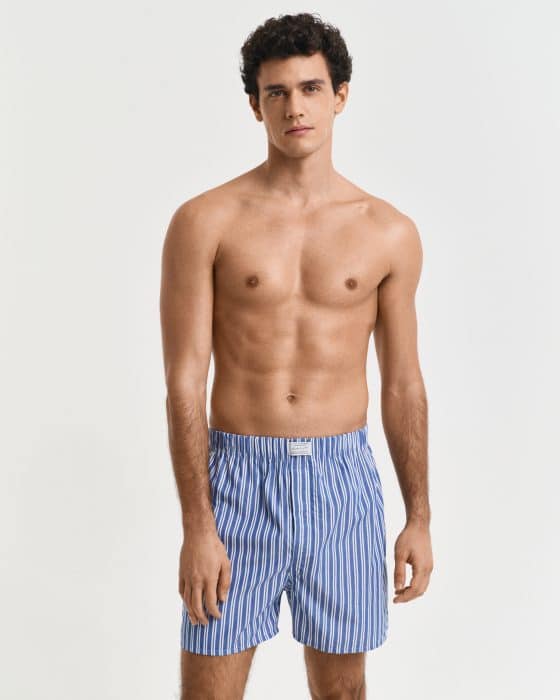 A shirtless man is wearing blue and white striped boxer shorts. He is standing against a plain white background.