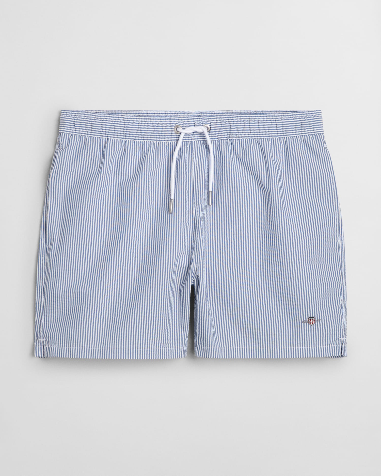 Blue and white striped swim shorts with an elastic waistband and white drawstring. The shorts have a subtle embroidered logo near the bottom hem on the left side.