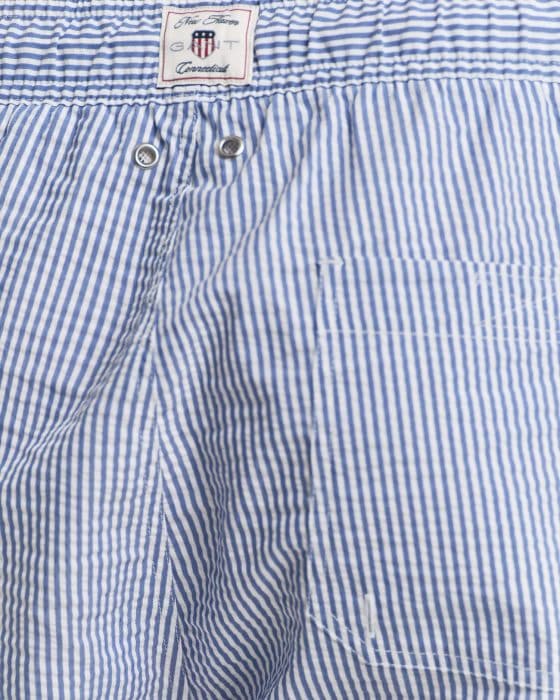 Close-up of blue and white striped fabric with a small pocket. A label at the top features text and a circular logo with stars and stripes.