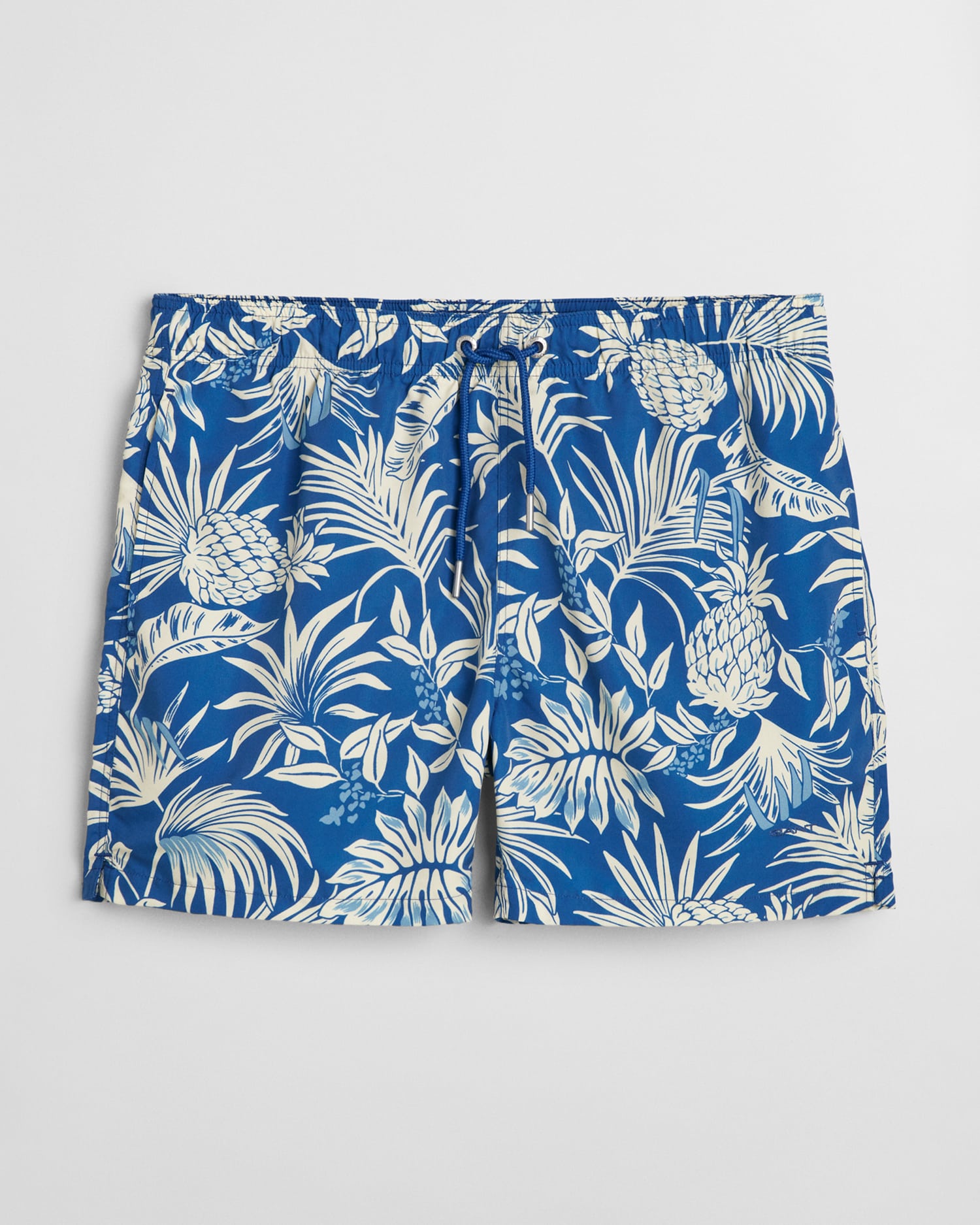 Blue swim shorts featuring a tropical pineapple and leaf pattern in white. The shorts have an elastic waistband with a drawstring.