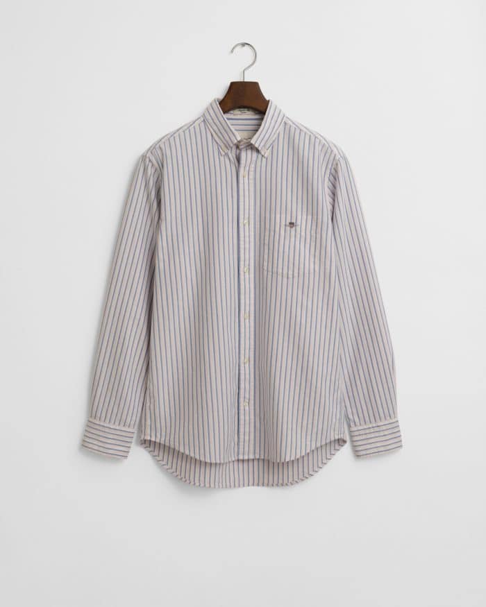 A long-sleeved button-up shirt with blue and white vertical stripes hangs on a wooden hanger against a plain white background. The shirt has a small embroidered emblem on the chest pocket.