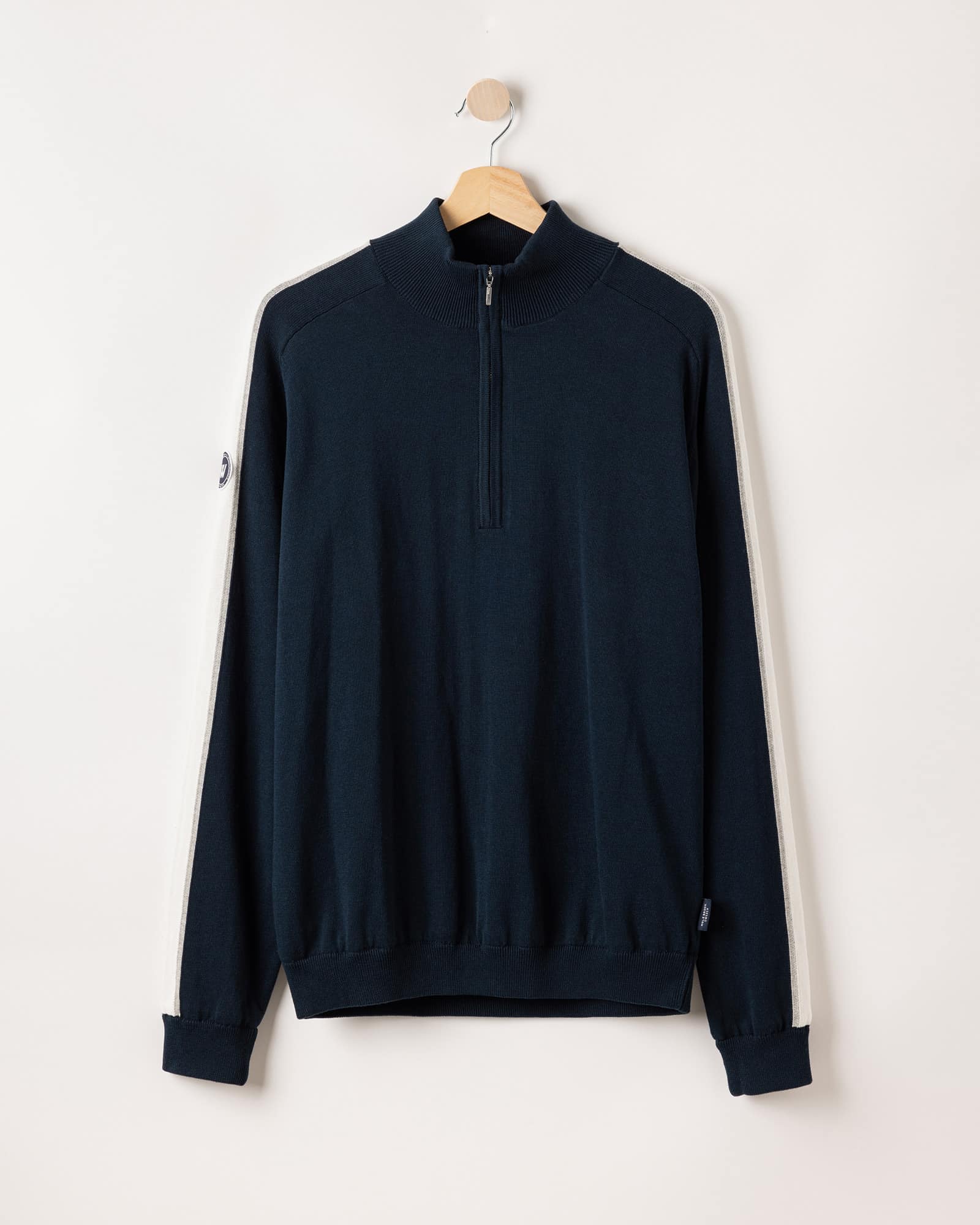 A navy blue pullover sweater with a half-zip front, hanging on a wooden hanger. The sweater features cream-colored stripes along the sleeves and a small logo patch on one sleeve.