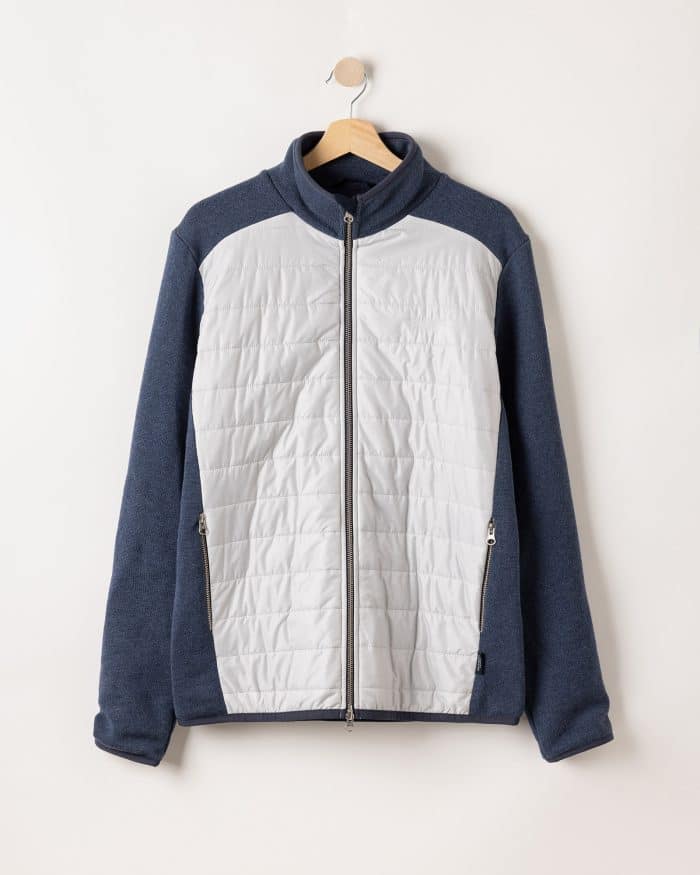 A jacket with a gray front and dark blue sleeves and back hangs on a wooden hanger against a plain white background. It features a zip-up front and two zippered pockets.