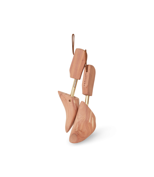 A pair of wooden shoe trees with a natural finish and metal springs, designed to maintain shoe shape, are shown against a plain black background.