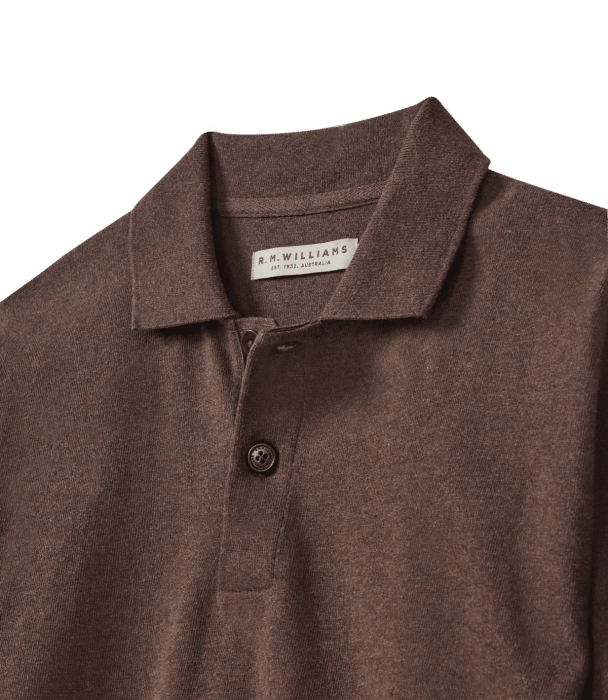 A close-up of a brown R.M. Williams polo shirt, showing the collar, two buttons, and a visible clothing label inside the neckline.