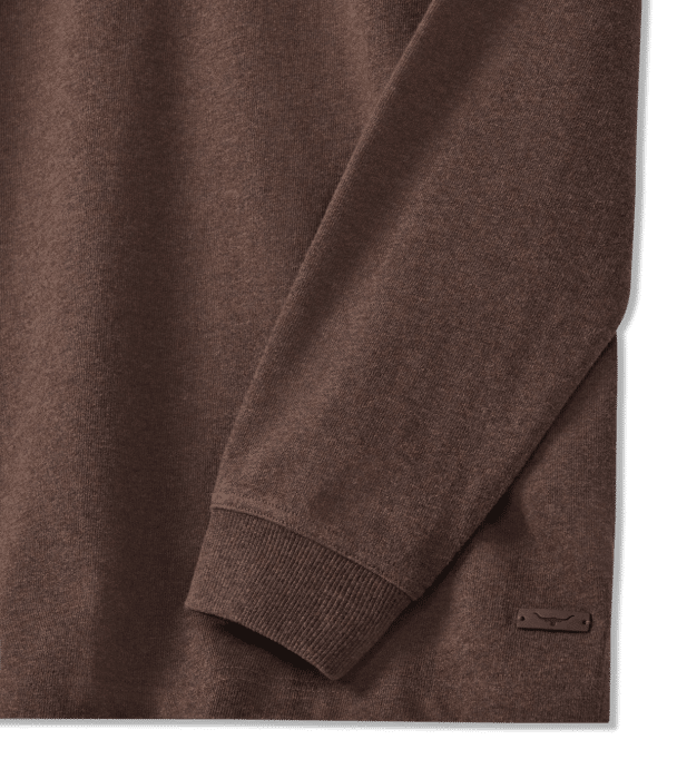 Close-up of a long-sleeve brown knit sweater, showing the cuff and part of the side. A small, rectangular brand tag is visible near the hem.