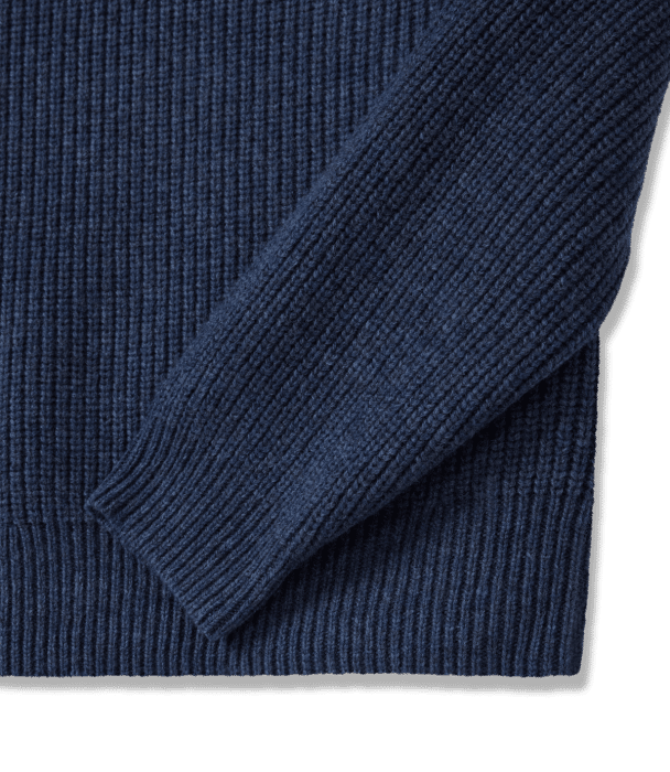 A close-up of a navy blue, ribbed knit sweater focusing on the sleeve and part of the body, showing the texture and pattern of the fabric.