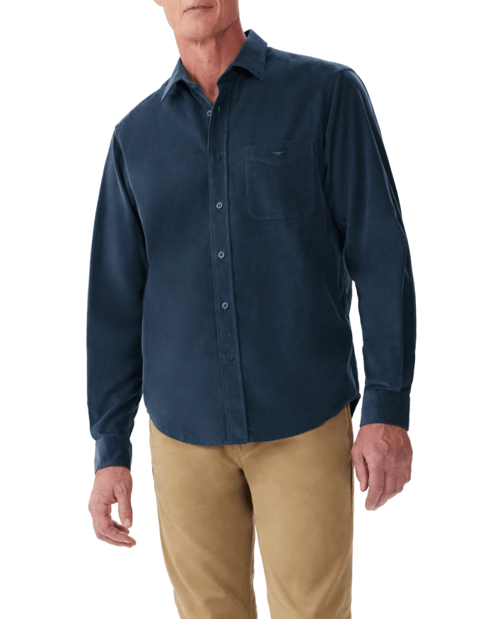 A man wearing a dark blue button-up shirt with a chest pocket and tan pants, standing against a plain background. His head is partially out of the frame.