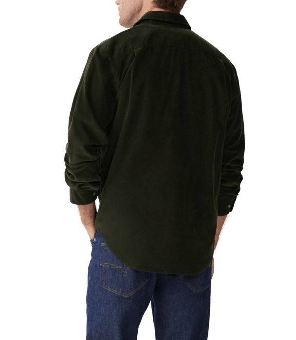 A person wearing a dark green long-sleeve shirt and blue jeans is seen from the back, with sleeves pushed up and hands resting in their pockets.