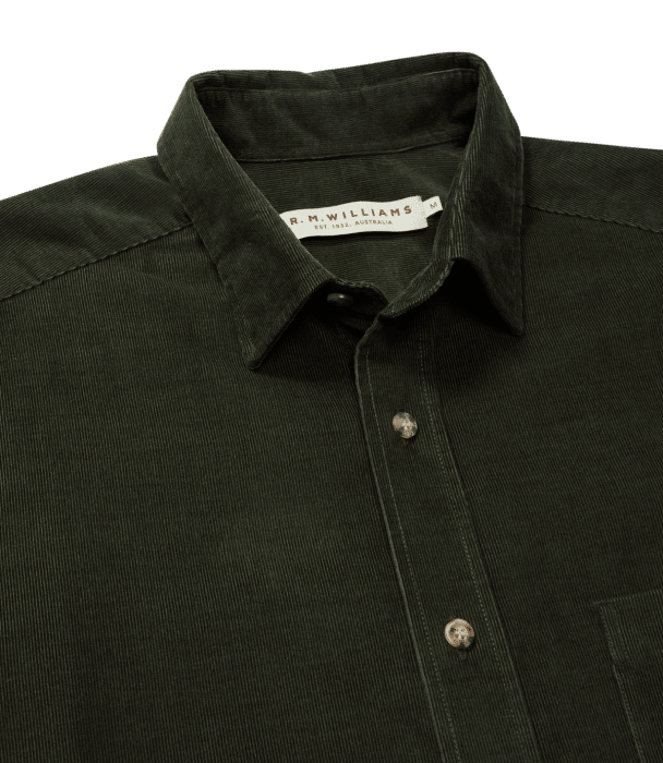 A close-up of a dark green corduroy button-up shirt with a collar and visible white label inside the neck that reads R.M. Williams.