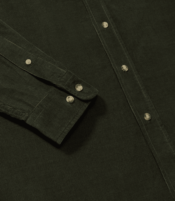 A close-up of a dark green corduroy shirt, showing the sleeve, cuff, and front buttons, all featuring light-colored buttons. The textured fabric and stitching details are clearly visible.