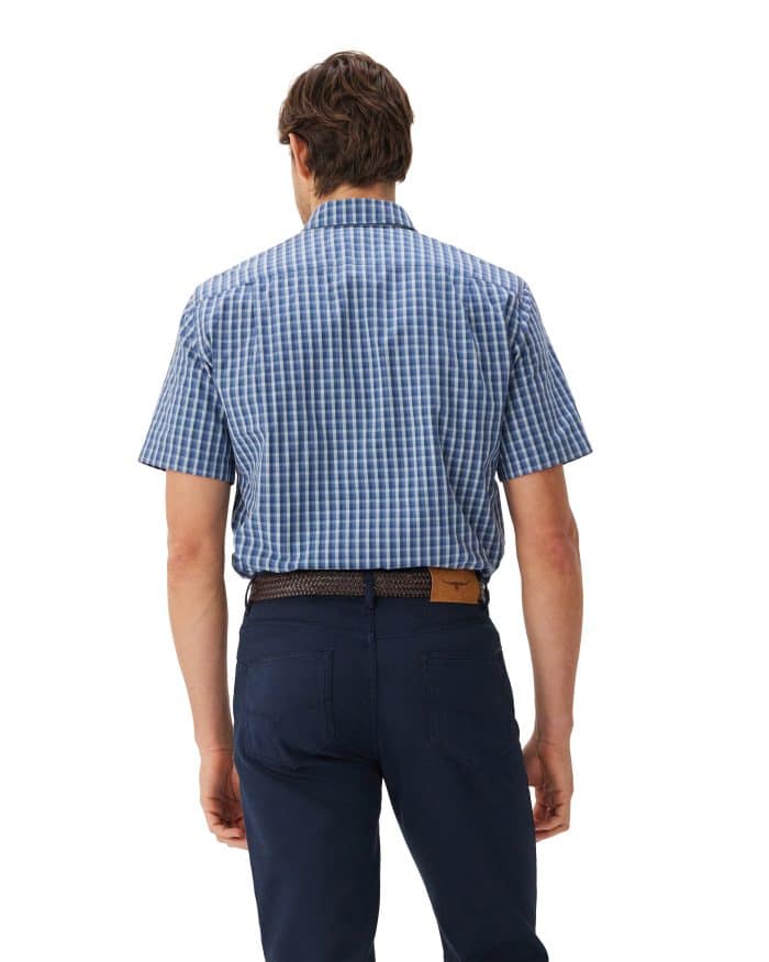 A man is standing with his back to the camera, wearing a blue and white checkered short-sleeve shirt tucked into dark blue pants and a brown belt.