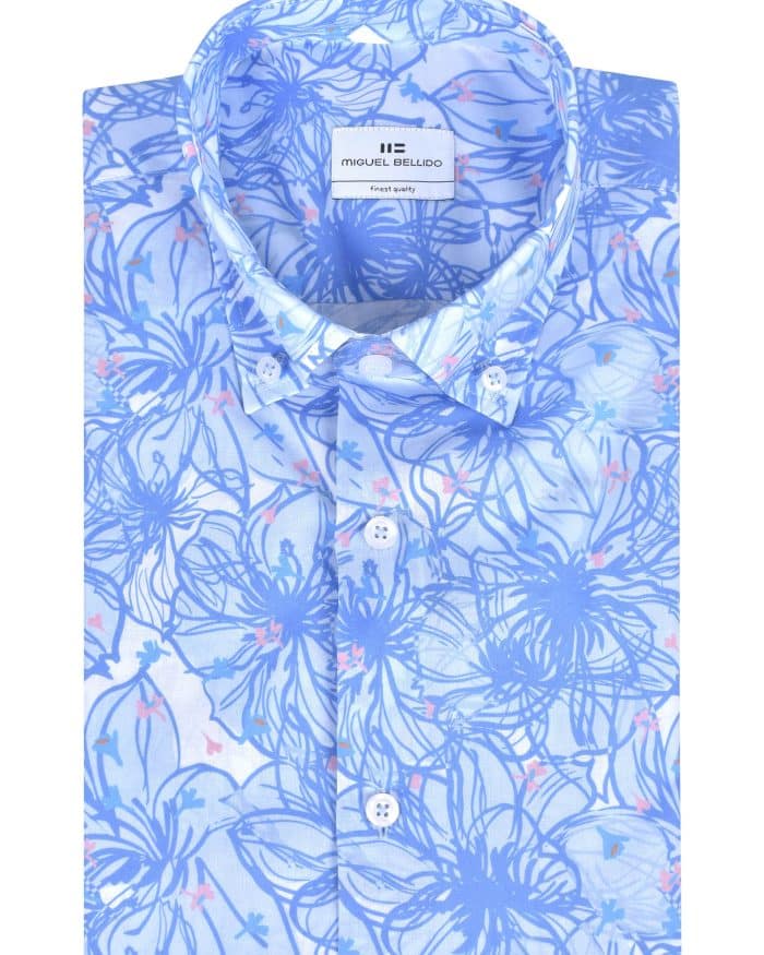A folded light blue dress shirt with a collar, featuring a white and blue floral pattern and white buttons. The inside label reads Miguel Bellido.