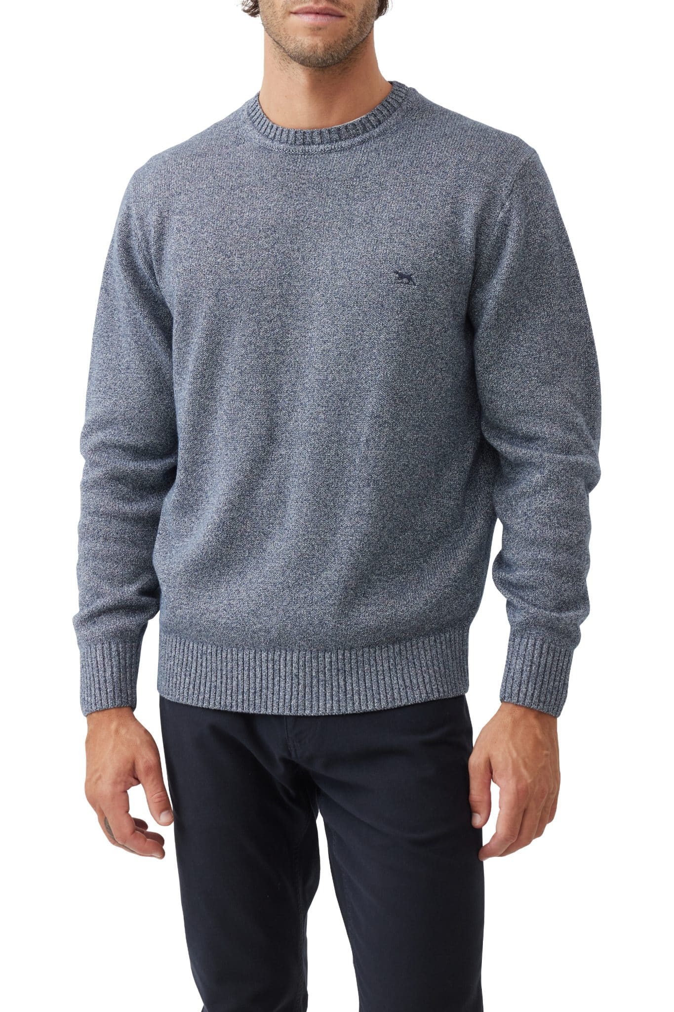 A man wearing a textured blue crewneck sweater with ribbed cuffs and hem, paired with dark pants, standing against a white background. His face is partially out of frame.
