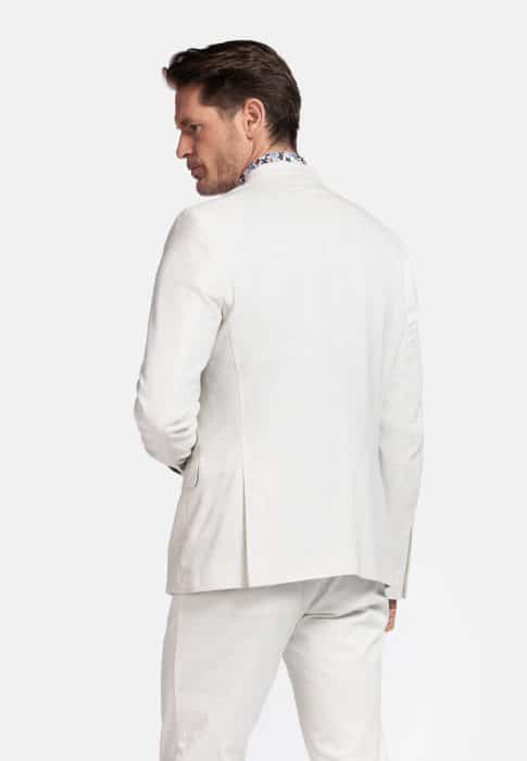 A man with short brown hair is shown from the back, wearing a light beige suit jacket and matching trousers. He is looking to his left over his shoulder against a plain white background.