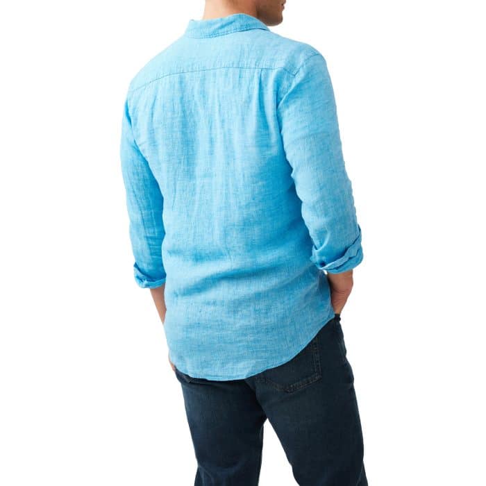 A man stands with his back to the camera, wearing a light blue long-sleeve button-up shirt and dark blue jeans.