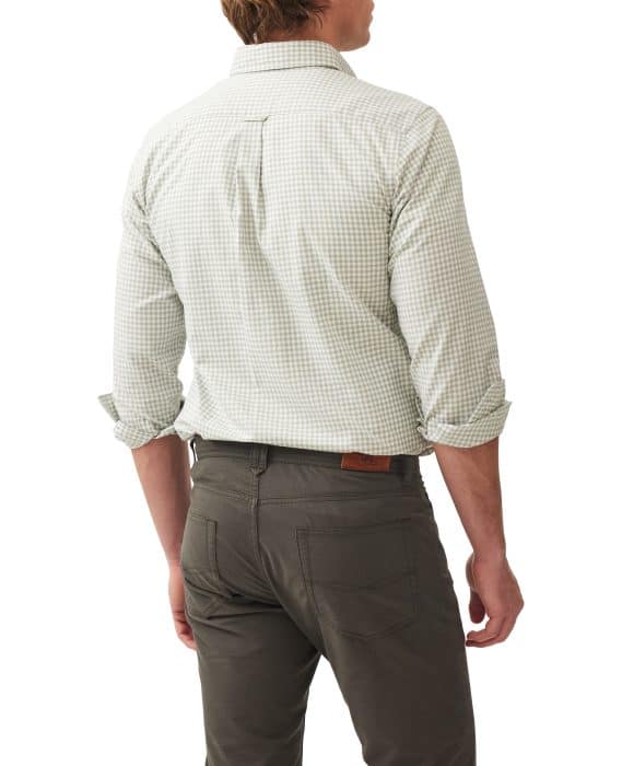 A man stands facing away, wearing a light green and white checkered long-sleeve shirt with rolled-up sleeves and gray pants. The background is white.