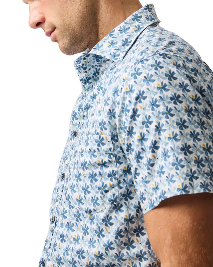 A man wearing a short-sleeve, button-up shirt with a blue, white, and yellow floral pattern, shown from the side against a white background.