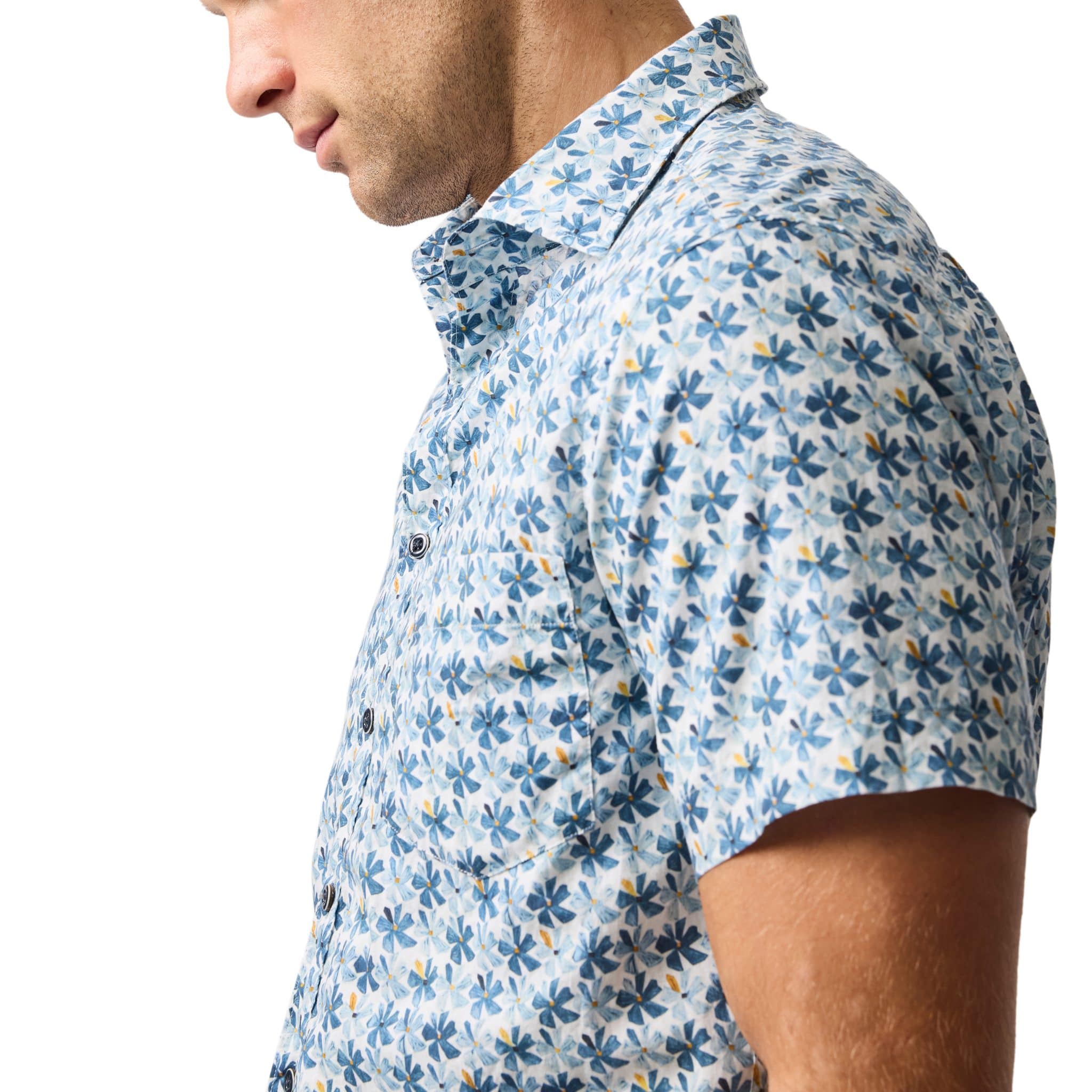 A man wearing a short-sleeve, button-up shirt with a blue, white, and yellow floral pattern, shown from the side against a white background.