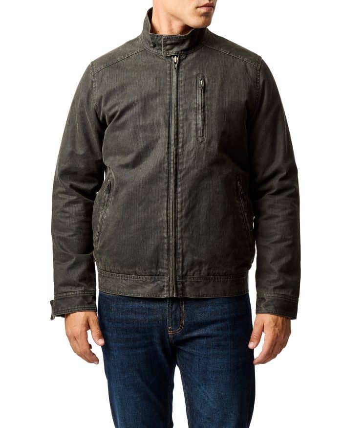 A man wearing a dark gray casual jacket with a stand collar, zippered chest pocket, and blue jeans, standing against a plain white background.