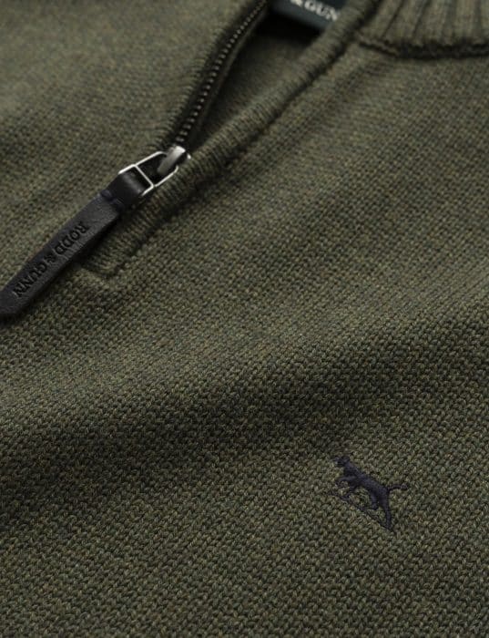 Close-up of a textured green sweater with a half-zip collar and a small embroidered black dog logo on the chest. The zipper pull has POLO GOLF written on it.