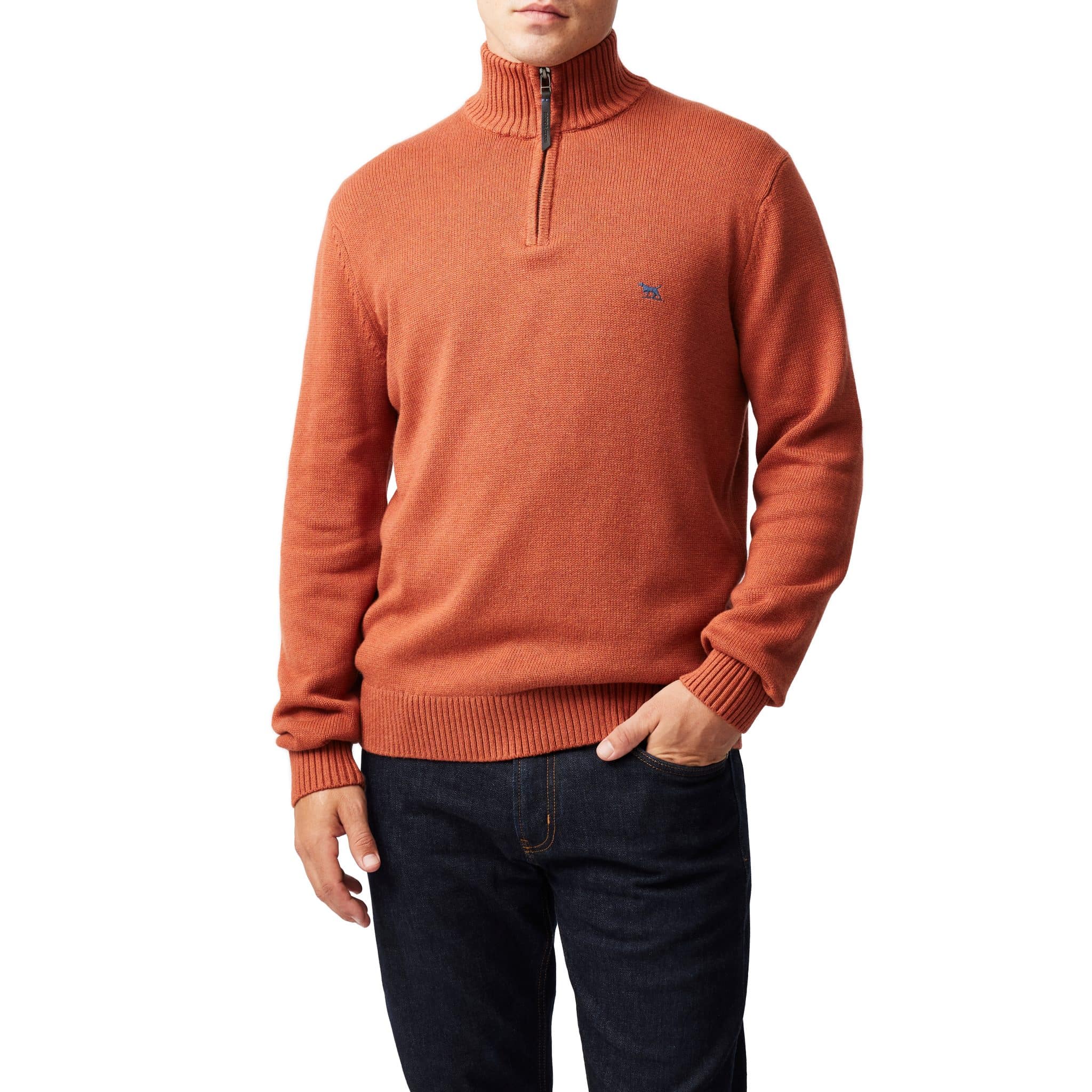 A person wearing an orange quarter-zip sweater with ribbed cuffs and hem, paired with dark blue jeans, standing against a plain white background.