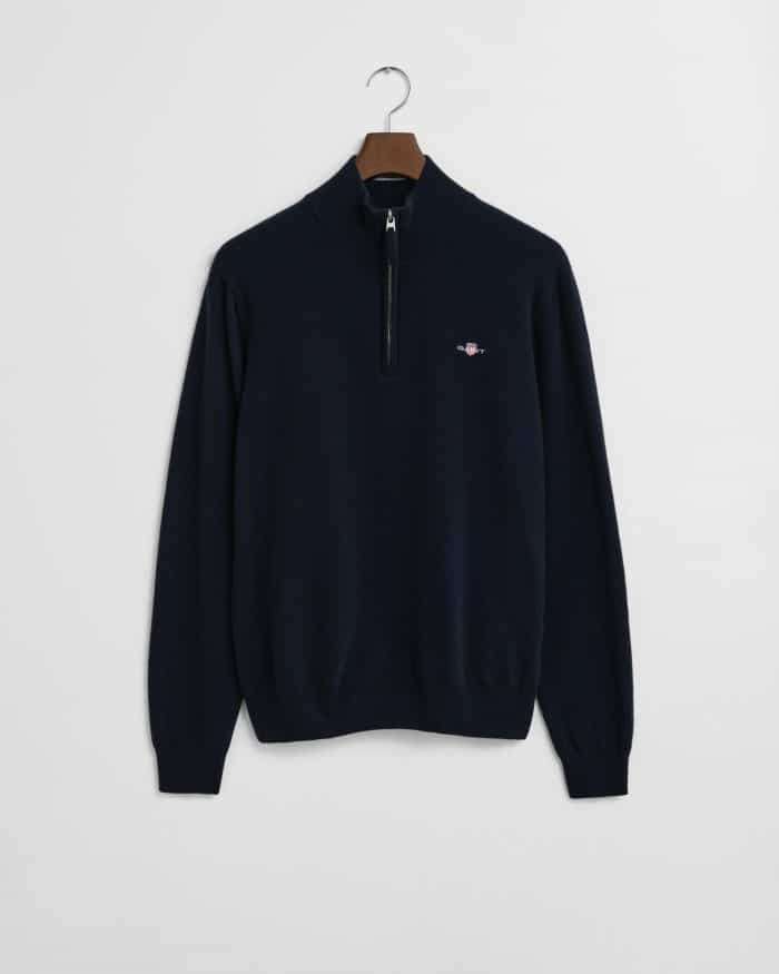 A navy blue quarter-zip sweater with a small embroidered logo on the left chest, hanging on a wooden hanger against a plain white background.