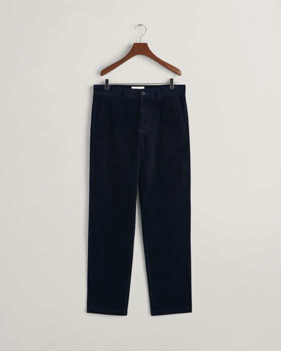 A pair of dark navy blue corduroy trousers hanging on a wooden hanger against a plain light gray background.