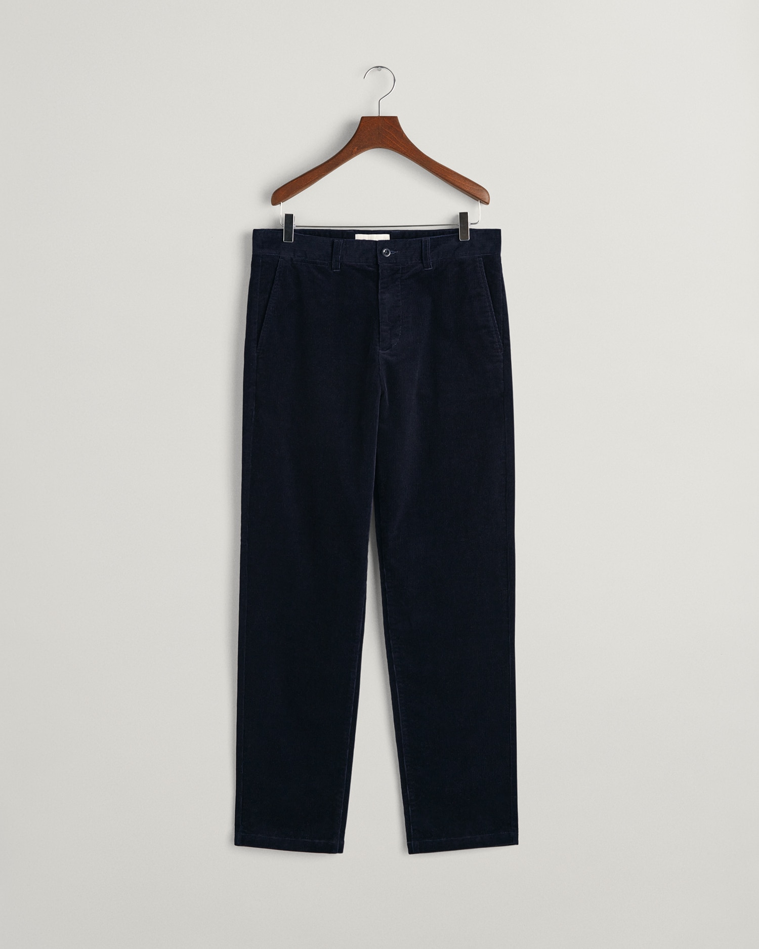 A pair of dark navy blue corduroy trousers hanging on a wooden hanger against a plain light gray background.