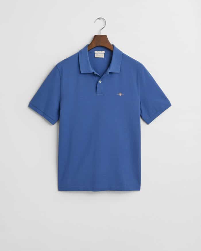 A blue short-sleeve polo shirt with a collar and buttons, displayed on a hanger against a white background. The shirt has a small embroidered logo on the left chest.