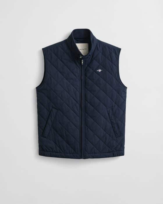 Navy blue quilted sleeveless vest with a stand collar, zip front, and two slanted pockets. The brand logo is embroidered on the left chest. The vest hangs against a plain white background.