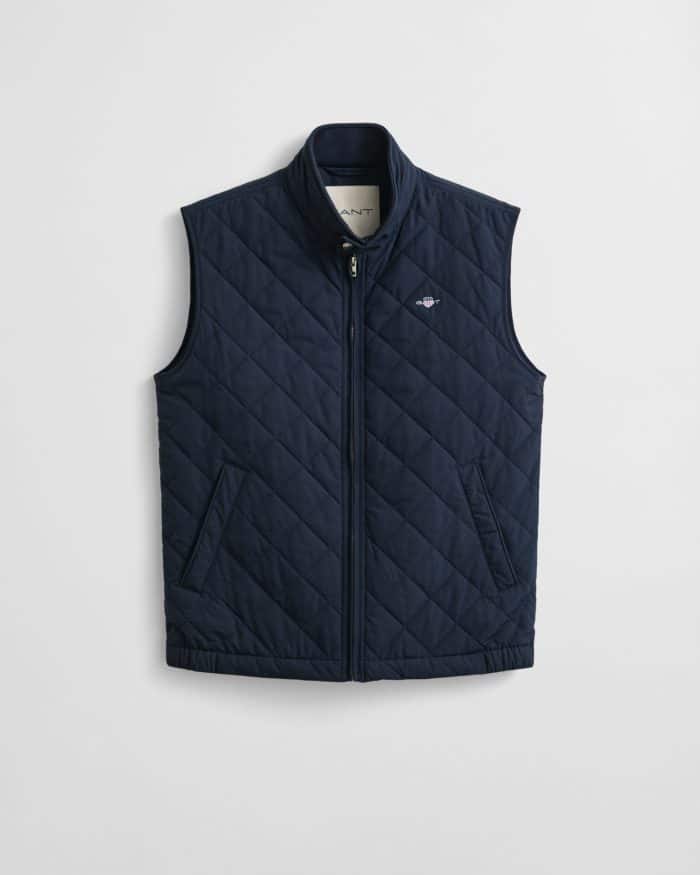 Navy blue quilted sleeveless vest with a stand collar, zip front, and two slanted pockets. The brand logo is embroidered on the left chest. The vest hangs against a plain white background.